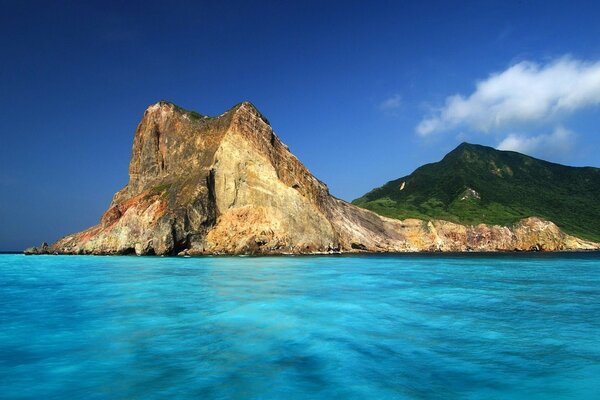 The sea with green mountains and a rock