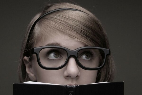 Foto de una chica con gafas sosteniendo un libro en sus manos