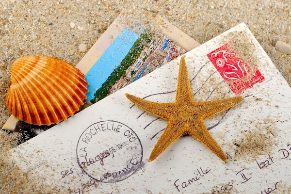 A letter with a postcard in the sand with shells