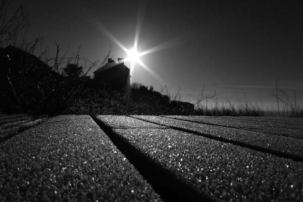 Black and white photo of the sun setting behind the house