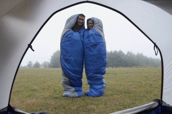 Um casal apaixonado em sacos de dormir fica em frente a uma tenda