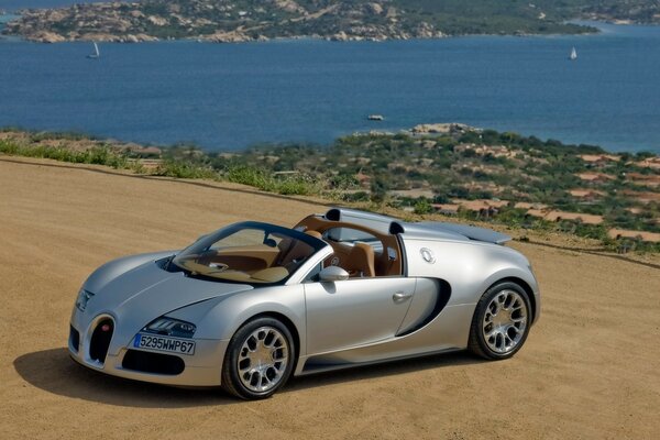 Coche deportivo bugatti gris en la playa junto al agua