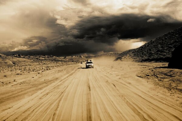 The car is moving through the desert on the sand against the background of sunset