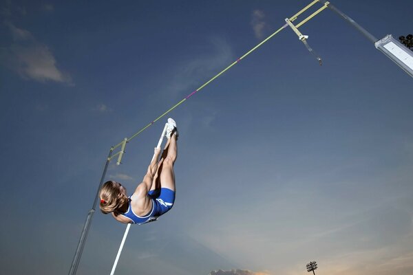 An athlete in a blue uniform performing a pole vault during an open-air competition