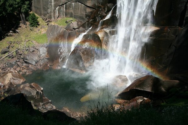 Wasserfall auf dem Hintergrund von Bergen , Regenbögen und grünen Bäumen