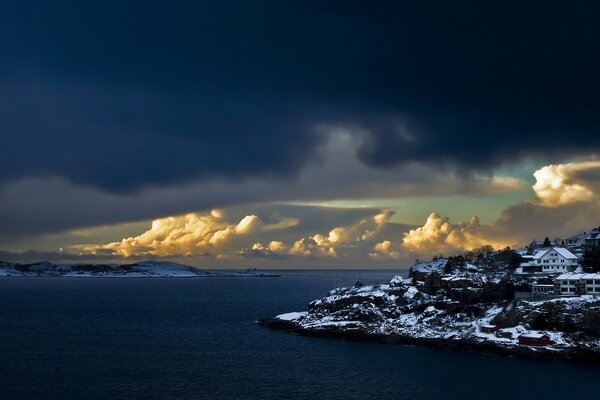 Häuser an der schneebedeckten Küste vor dem Hintergrund riesiger Wolken