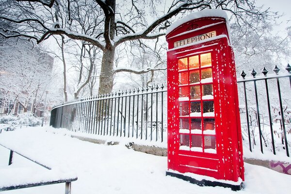 A bright telephone booth in the middle of a snowy street