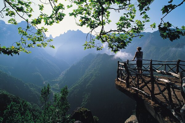 A girl stands on the edge of an observation deck in the mountains