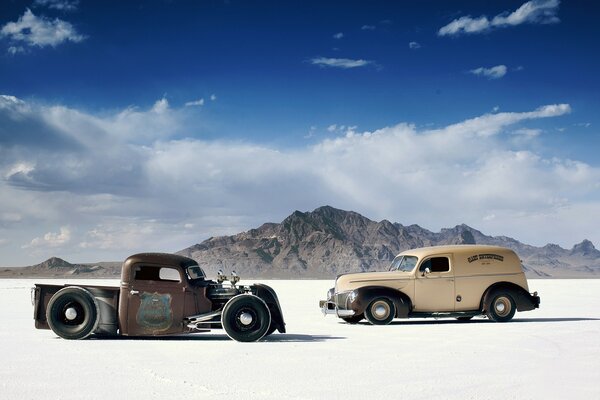 Two retro cars stand in the desert against the backdrop of mountains