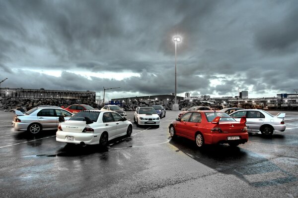 A group of mitsubishi cars standing around on an asphalt platform against a stormy sky