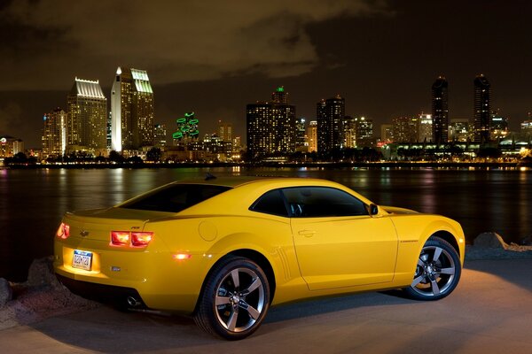 Chevrolet giallo con fari accesi sullo sfondo della città notturna