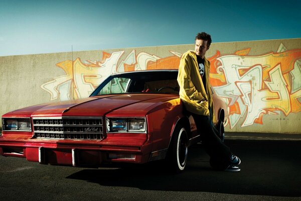 Joven al lado de un coche rojo