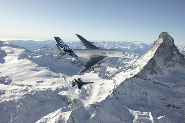 Aereo di linea e caccia che volano sopra le montagne innevate