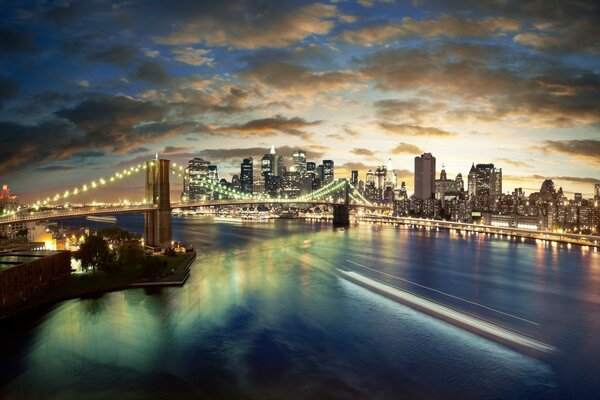 Vista noturna da ponte iluminada sobre o rio com nuvens no céu