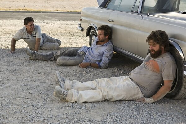 Three men lay down behind the car