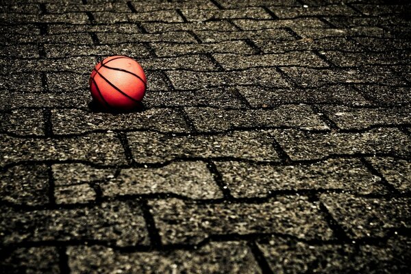 An orange basketball lying on a stone pavement