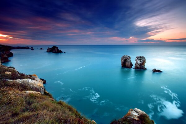 منظر لسطح البحر المتدفق وراء حافة أفق المساء ، ينظر صخران وحيدان إلى بعضهما البعض