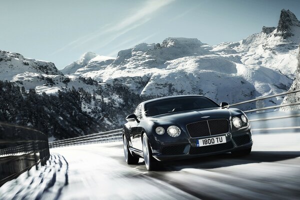 Schwarzer Bentley im Winter auf der Autobahn. Vor dem Hintergrund der Berge und des Himmels