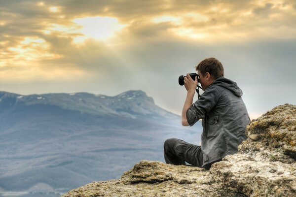 Le gars est assis sur un rocher et tire sur la caméra les rayons du soleil qui passent à travers les nuages