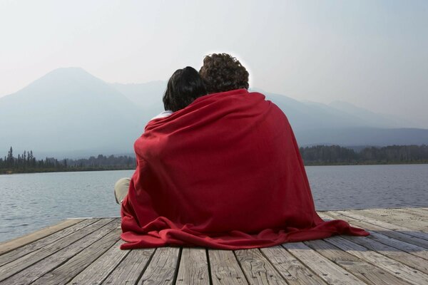 Two lovers on the pier under a red blanket