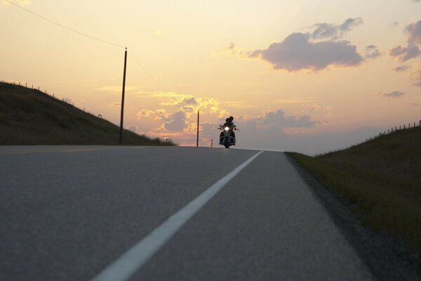 一对夫妇的人骑摩托车沿着道路进入夕阳