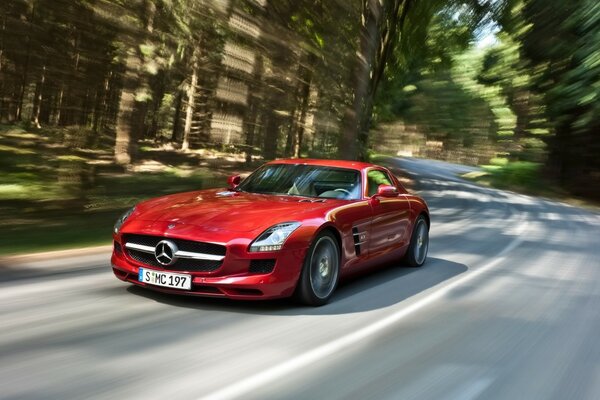 A red car is driving along a forest road