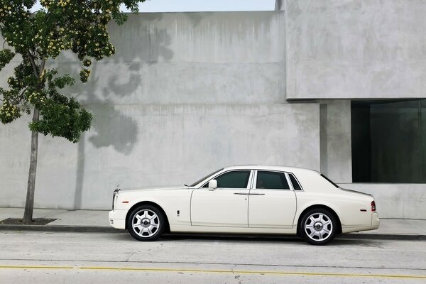 A white car is parked in front of a building with a gray facade