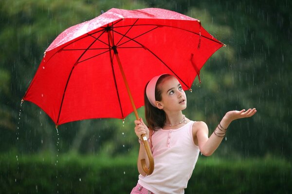 Nettes kleines Mädchen mit einem roten Regenschirm im Regen