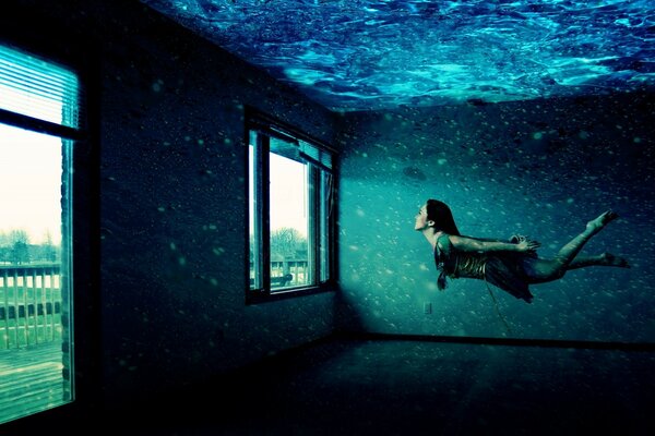 A girl swims underwater in a room with windows