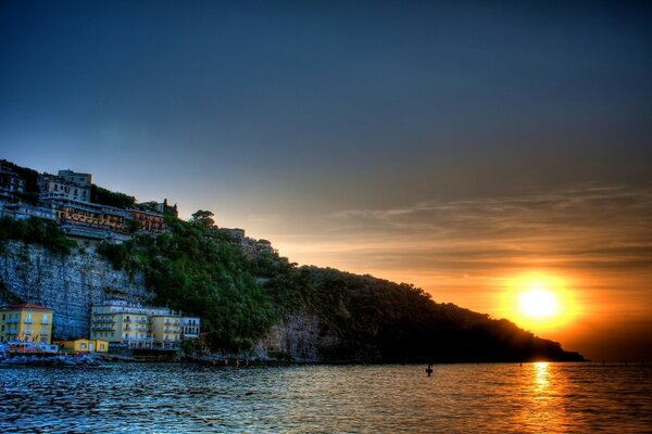 Puesta de sol junto al mar con casas en las rocas