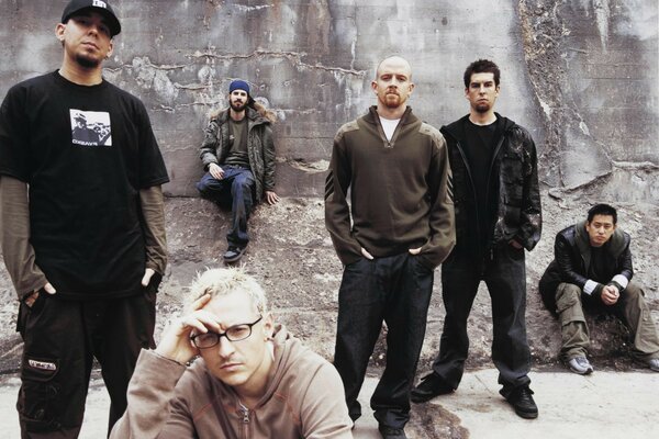 A group of guys are standing and sitting near a gray wall