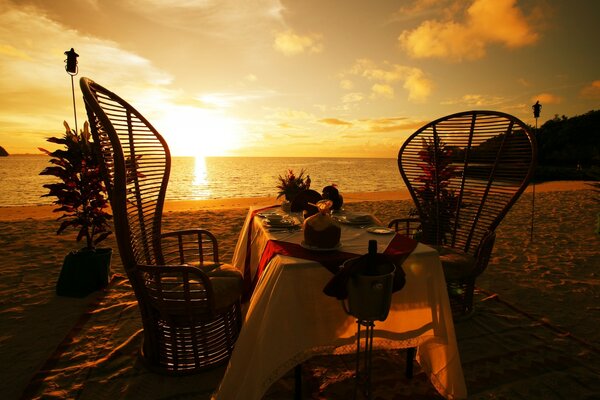 Abendessen für zwei Personen am Strand bei Sonnenuntergang am Meer