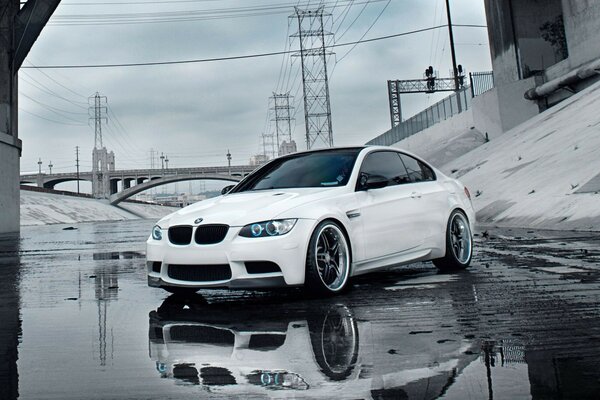 A sporty white car is reflected in a puddle