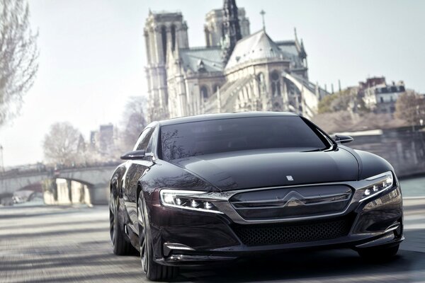 A black car drives past an old building