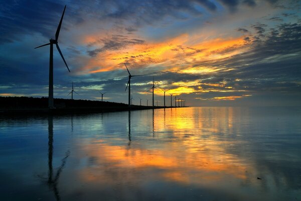 Pôr do sol refletido na água com moinhos de vento ao longo da Costa