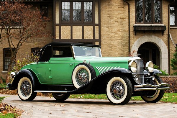 A passenger car of the early 20th century green with a convertible top and two passengers