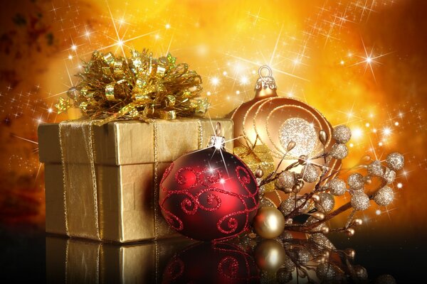 Regalo di Natale avvolto in carta dorata e un paio di palle di Natale su uno sfondo di luci