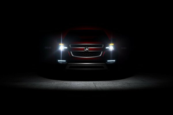 A red foreign car is standing in the dark with its headlights on