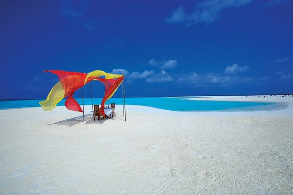 Romantic table on a deserted beach with white sand and blue sea