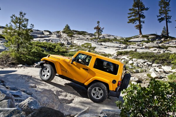 Yellow jeep makes its way over rocks in the open air