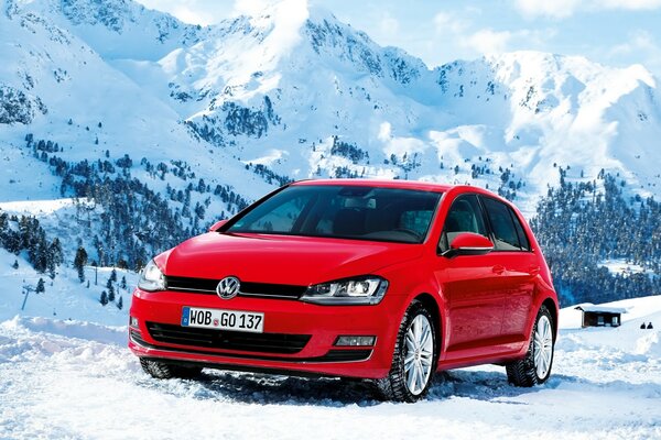 A red Volkswagen car stands on the snow against the background of mountains