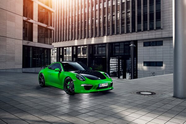 A green Porsche on the sidewalk near a modern building