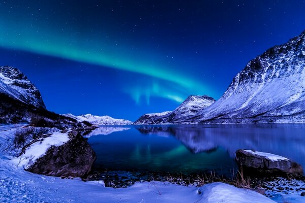 Paesaggio artico di un lago di montagna ghiacciato in coste innevate sotto il cielo con l aurora boreale