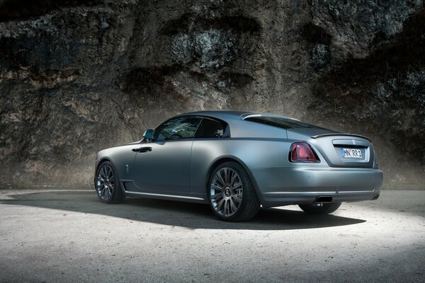 A graphite-colored rolls royce car stands on the sidewalk