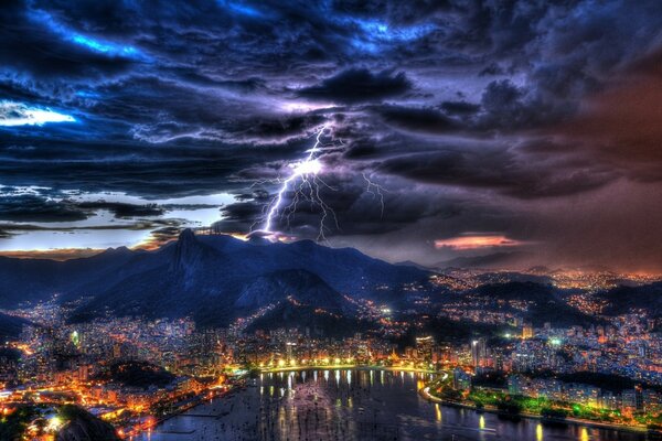 Bright lightning in the night sky over the city at the foot of the mountain