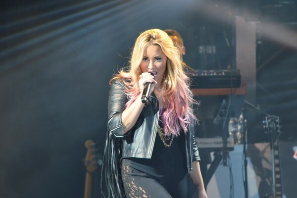 Foto de una rubia cantando en un concierto con un micrófono