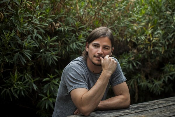 A man is sitting against a background of trees