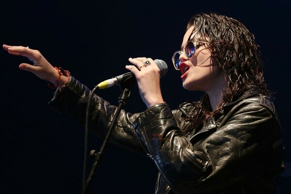 Intérprete de pelo oscuro con chaqueta de cuero y gafas canta en el micrófono