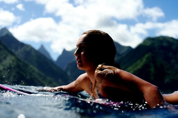 A girl swims on a board against the backdrop of high mountains