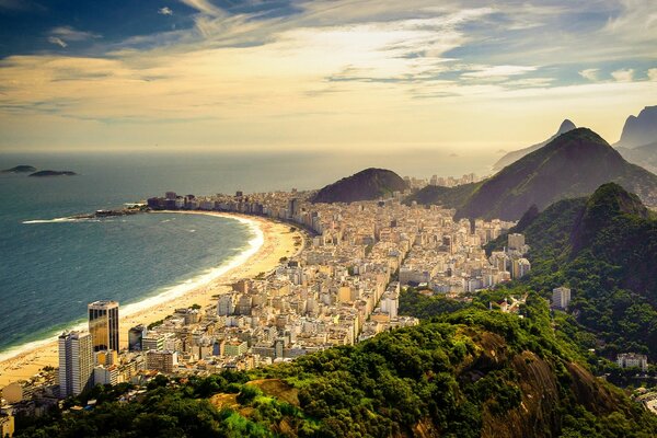 Longa praia de areia na costa com edifícios altos e montanhas